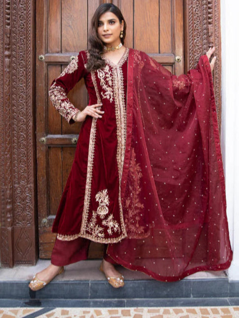 Woman in a red traditional outfit standing in front of a wooden door.